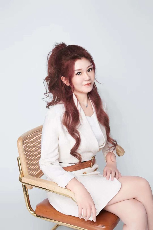 Stella Zhou 的形象照：身穿白色西装，坐在藤编椅上